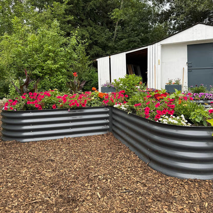 Two metal raised garden beds with flowers in front of a white shed.
