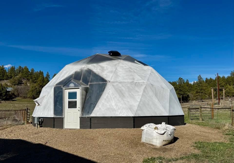 Arctic Acres Growing Dome greenhouse exterior in a rural setting under a clear blue sky.